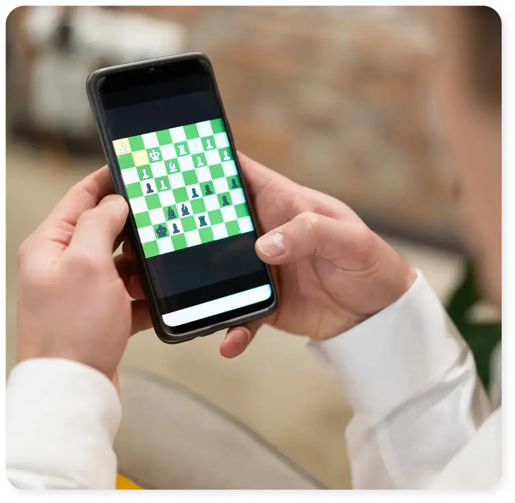 A man plays chess at home on his laptop, in a cozy setting with the chess pieces beside him.