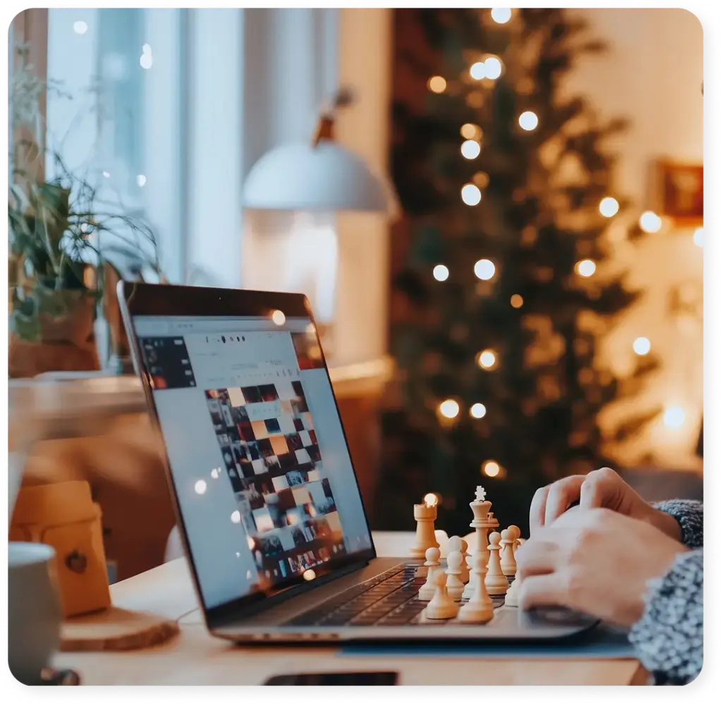 A man plays chess at home on his laptop, in a cozy setting with the chess pieces beside him.